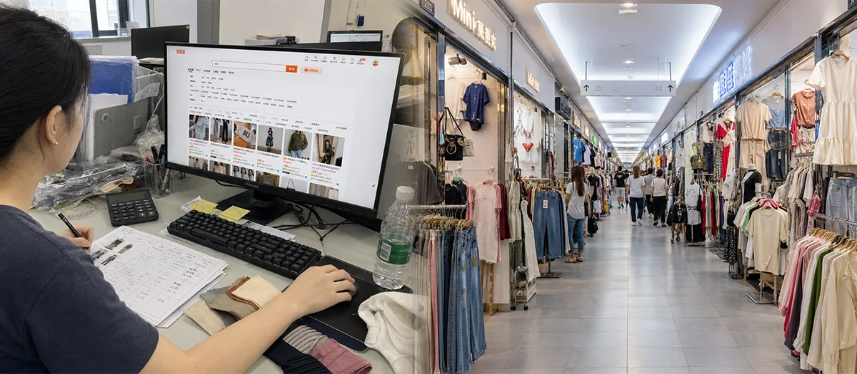 A buyer at a monitor showing the 1688 wholesale site, beside a corridor of garment stalls in a wholesale market.