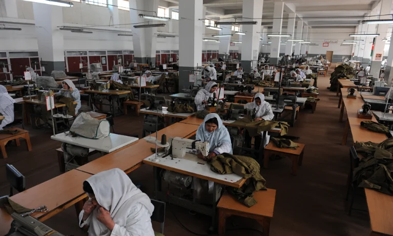 Machinists at industrial sewing machines on a garment factory floor.