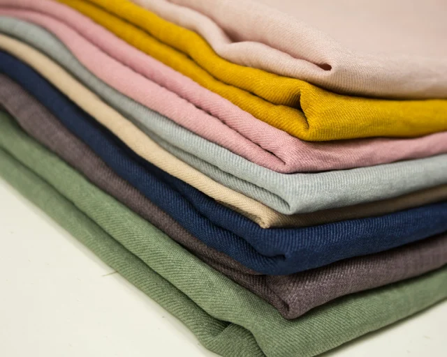 Folded linen fabrics in green, navy, pink, yellow and cream stacked on a table.