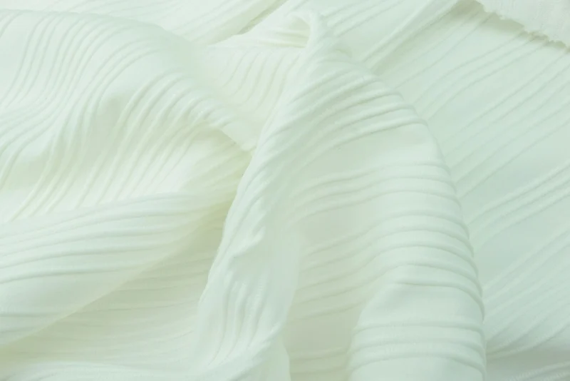 Close view of narrow pleats pressed into pale fabric.