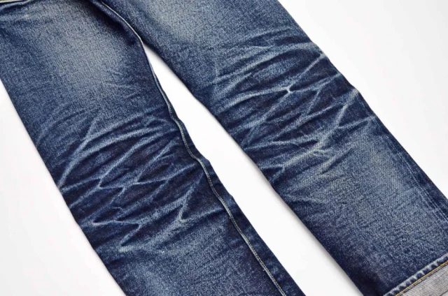 The legs of dark blue jeans with pale crease lines across the thighs.
