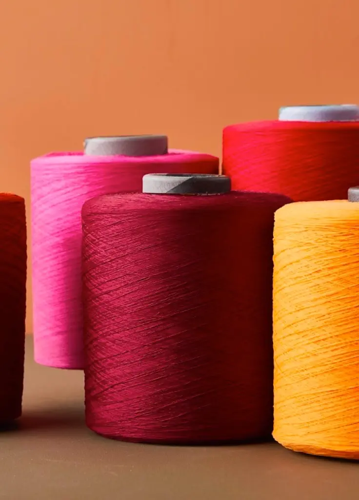 Cones of pink, red, cream and orange polyester filament yarn.