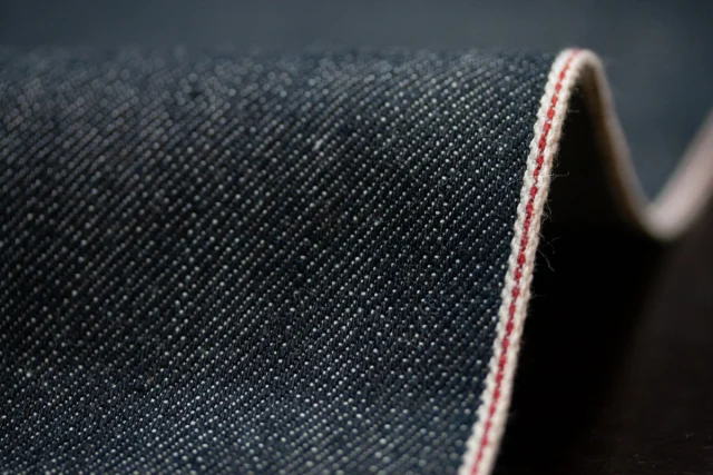 Dark indigo denim folded over to show its white selvedge edge.
