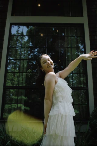 A woman in a white tiered chiffon dress with her arms raised.