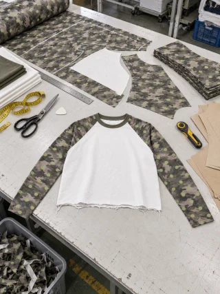Camouflage sleeve panels laid out in pairs around the white body pieces on a cutting table.