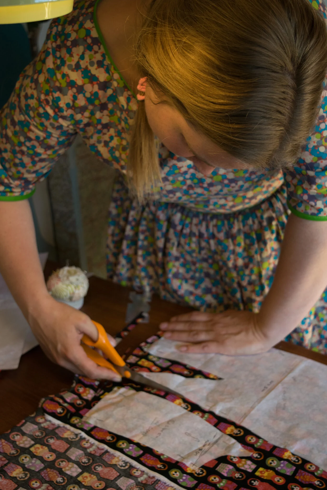 Paper pattern pieces laid on printed fabric while the fabric is cut around them with orange scissors.