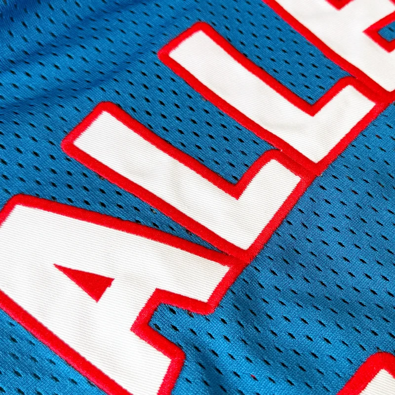 White twill letters edged in red, stitched onto teal jersey mesh.