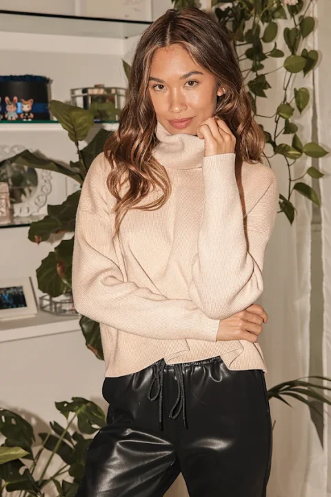 A woman in a beige cowl-neck sweater with a softly folded neckline.
