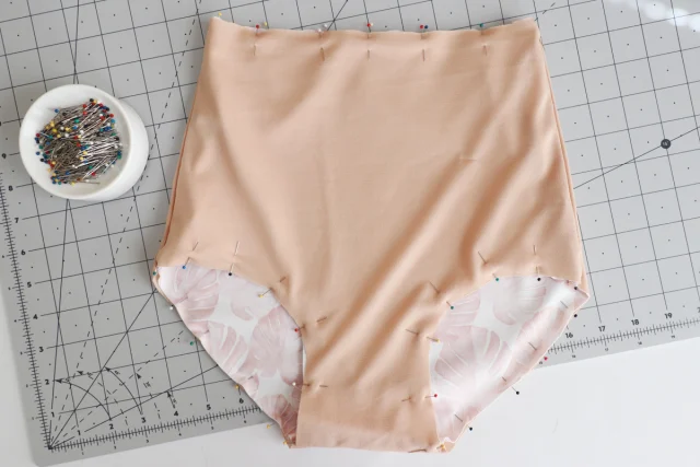 A bikini bottom with its shell and lining pinned together on a cutting mat.