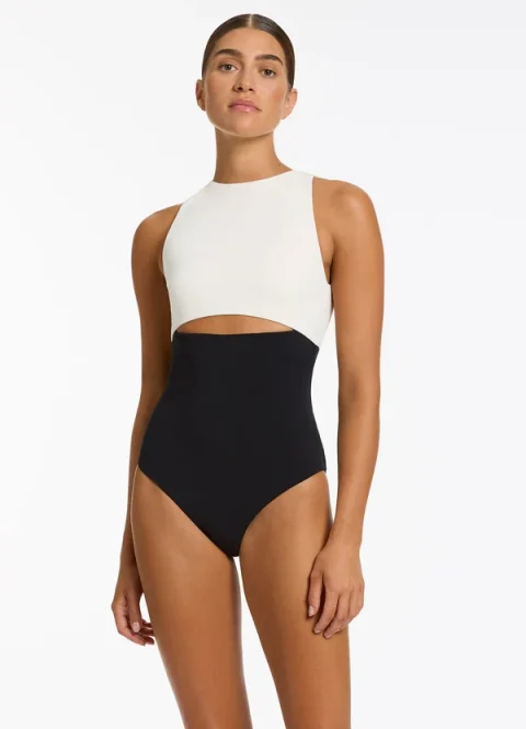 A model in a cream and black one-piece swimsuit with a cutout under the bust.
