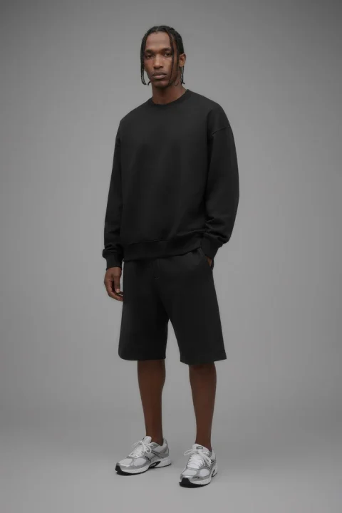 A man in a black oversized crewneck sweatshirt and black shorts.
