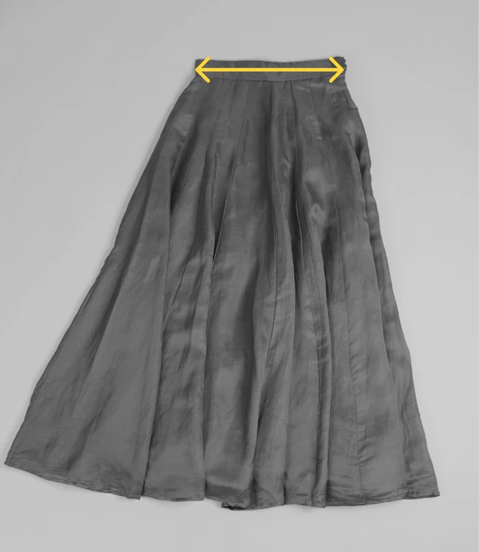 A black pleated skirt laid flat with a marker across the waistband.