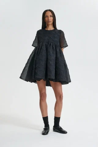 A black textured babydoll mini dress with short sleeves and a wide gathered skirt.