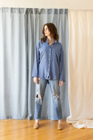 A blue button-front tunic blouse with chest pockets and a long curved hem, over faded jeans.