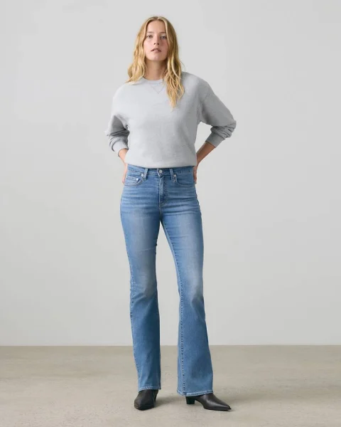 A woman in blue flare jeans, a gray sweatshirt and black heeled boots.