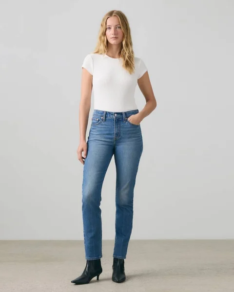 A woman in mid-blue slim jeans, a white T-shirt and black ankle boots.