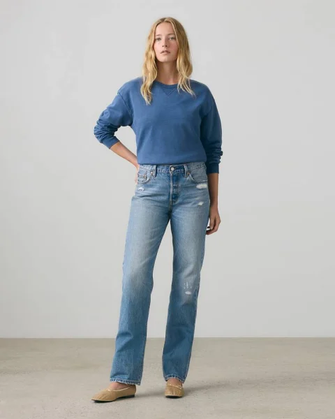 A woman in light blue straight-leg jeans, a blue sweater and tan flats.