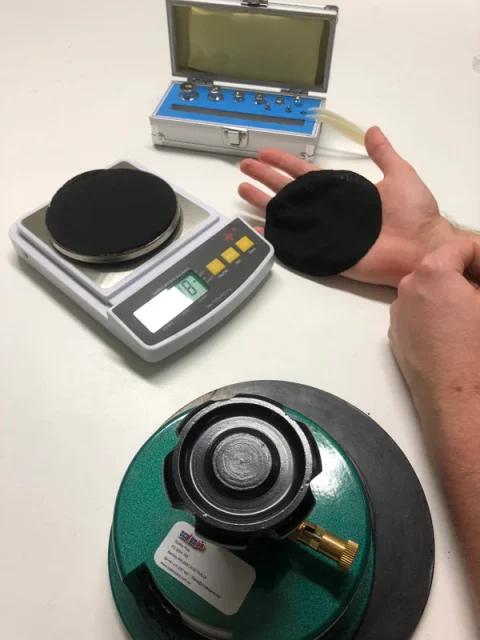 Circular fabric samples on a digital scale beside a round sample cutter.
