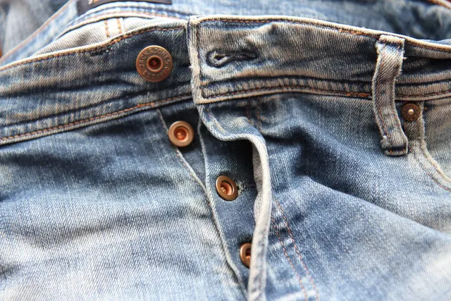 Close view of a button fly with copper buttons on light blue jeans.