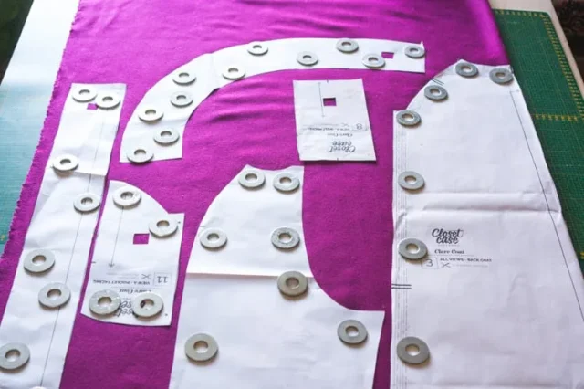 Paper pattern pieces and pattern weights laid out over magenta shell fabric.
