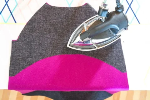 Dark fusible interlining being pressed onto a magenta coat panel with a steam iron.