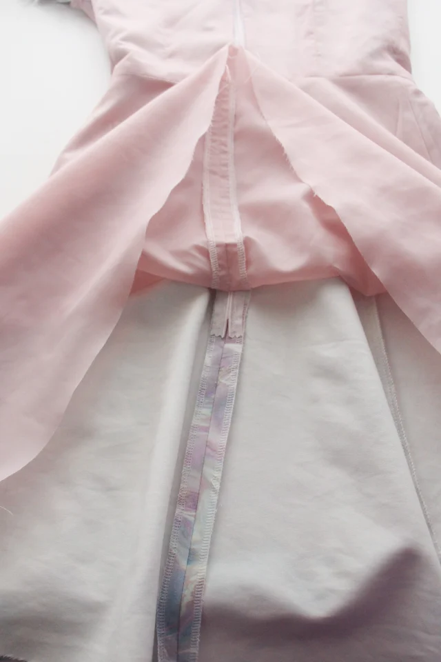 The inside of a white dress turned back to show a pale pink bodice lining and the center-back zip.