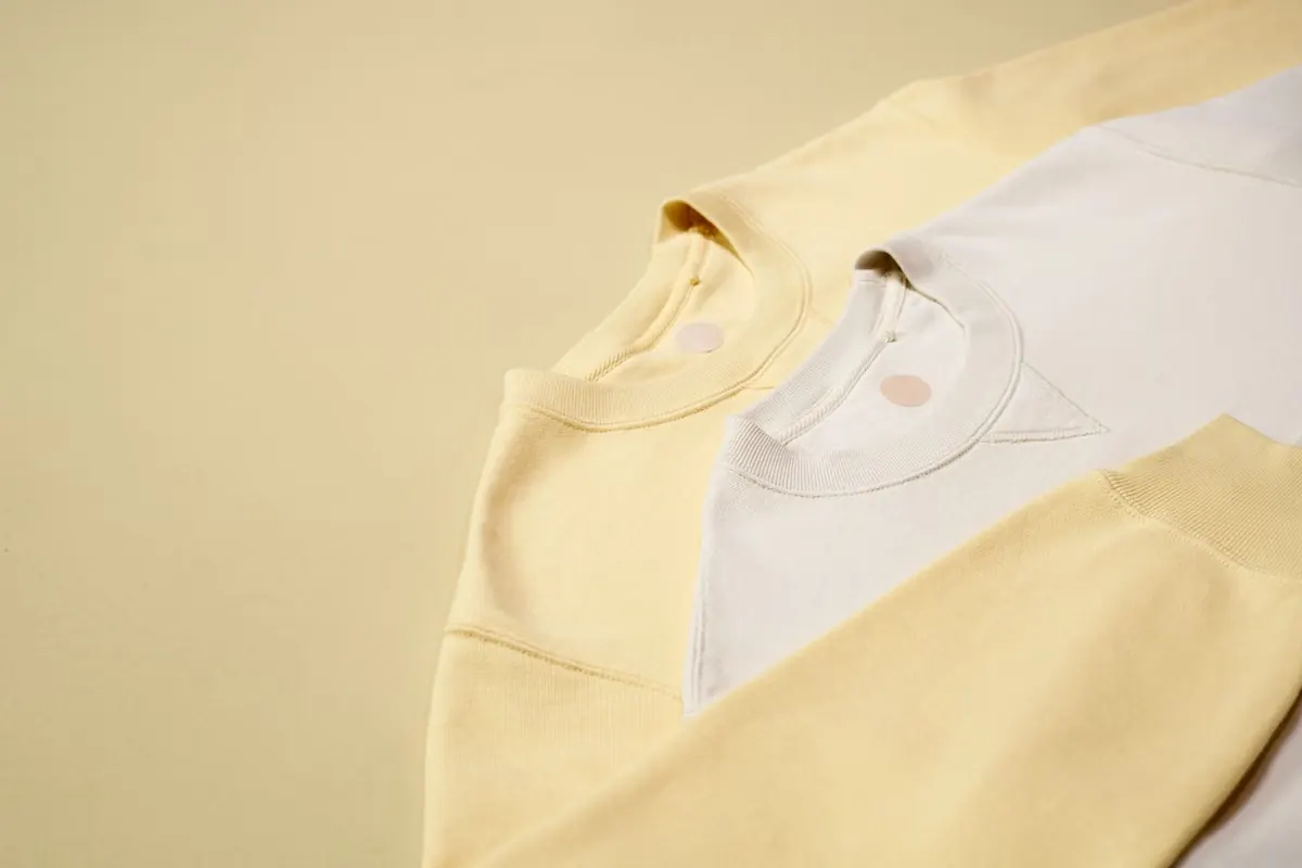 Cream and pale yellow crewneck sweatshirts folded in a stack.