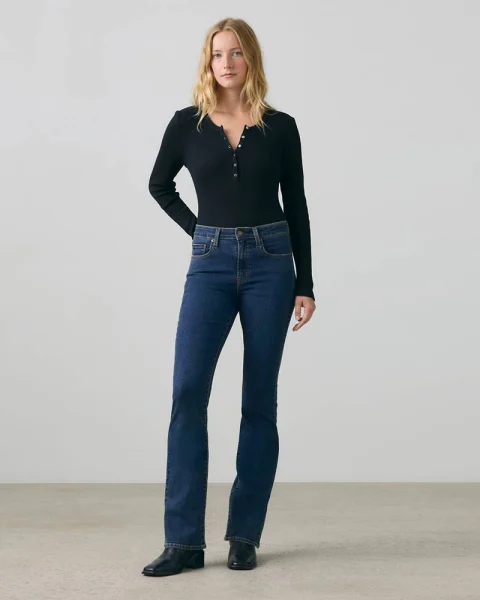 A woman in dark blue bootcut jeans, a black top and black boots.
