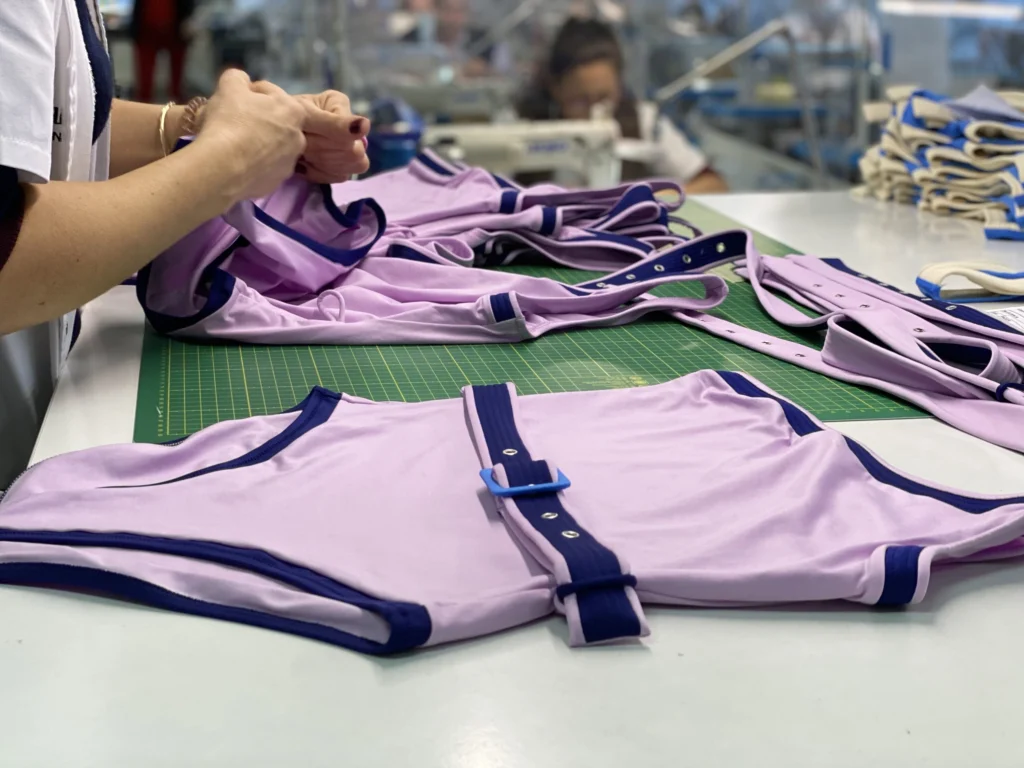 Finished lilac one-piece swimsuits with navy trim being checked on a factory worktable.