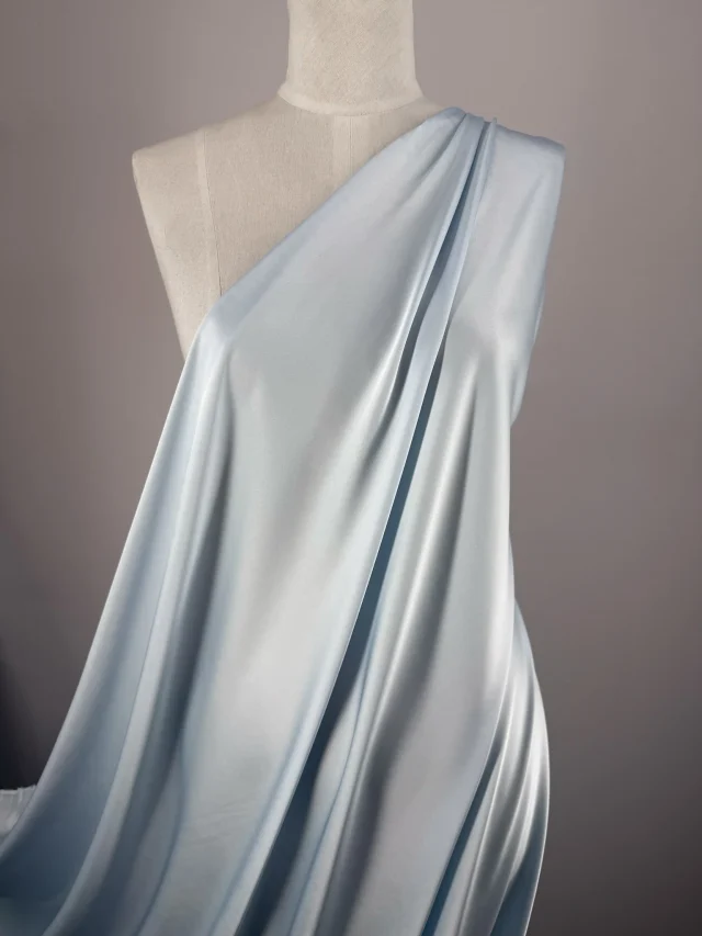 Pale blue satin draped from one shoulder of a dress form and falling to the floor in soft folds.