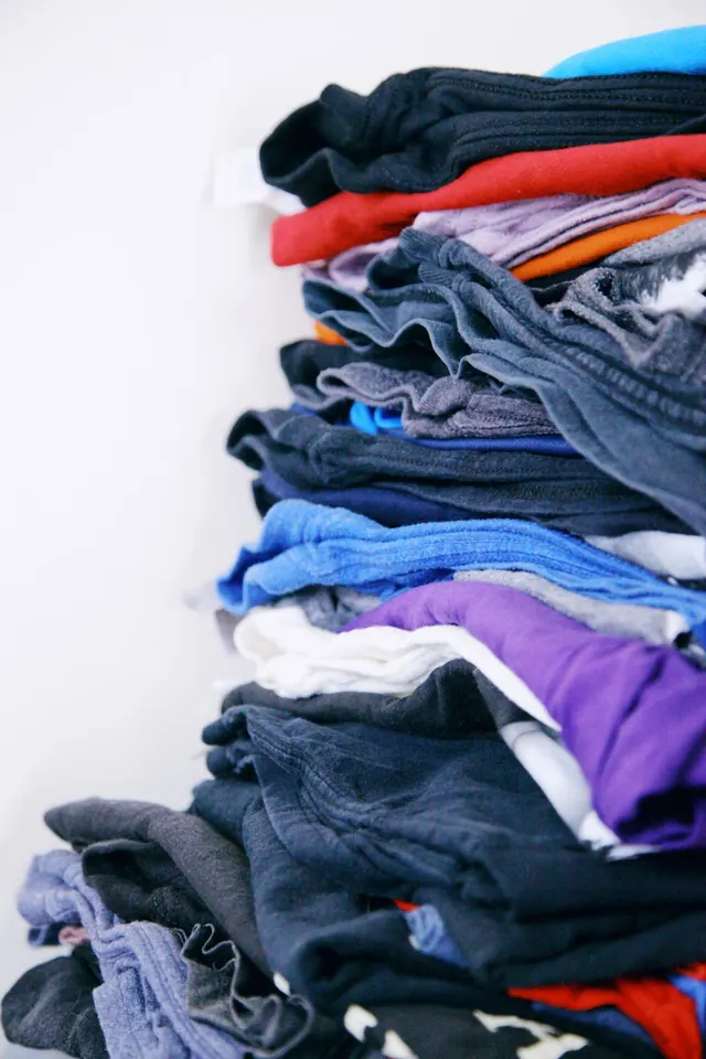 A stack of folded garments in blue, gray, red and purple.