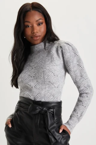 A woman in a grey textured sweater with a short standing collar and puffed shoulders.