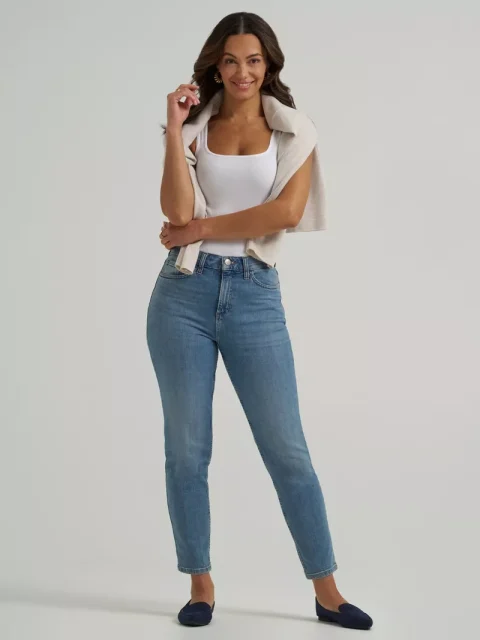A woman in high-rise mom jeans and a white top, with a sweater tied over her shoulders.