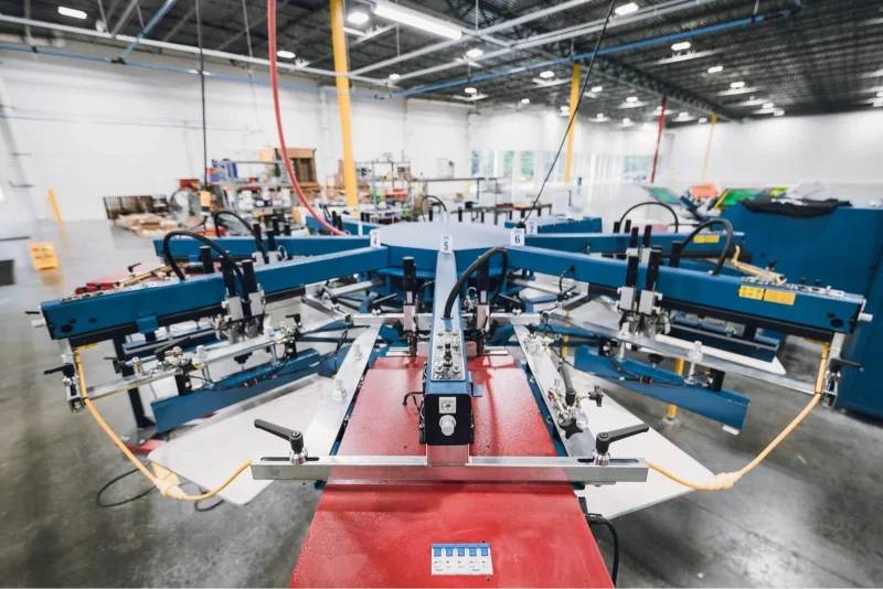 A carousel screen-printing press in a factory. Its print heads stand in a ring around a red pallet.