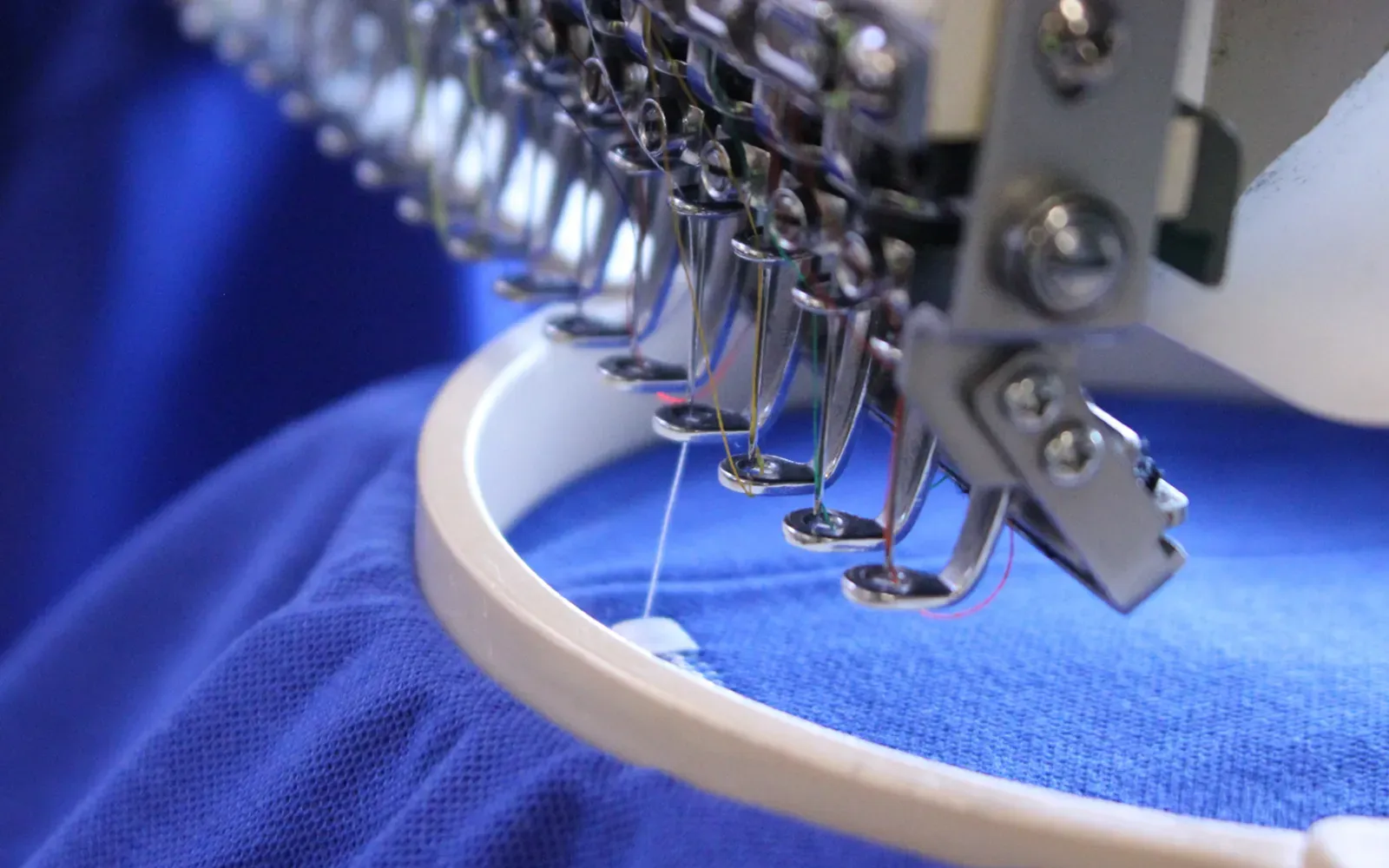 A multi-needle embroidery machine stitching through blue fabric held in a hoop.