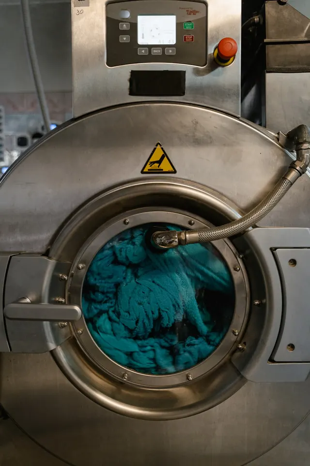 Teal garments tumbling in the drum of an industrial washing machine.