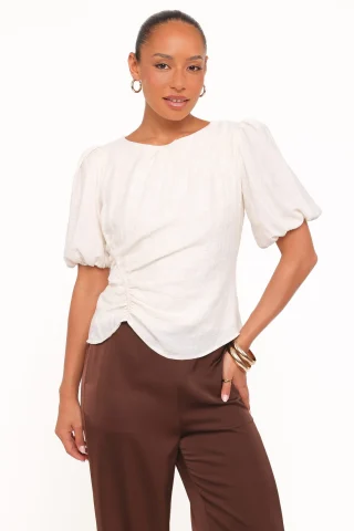 An ivory blouse with short rounded puff sleeves, a gathered front and a curved hem.