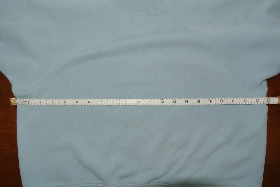 A light blue crewneck sweatshirt laid flat with a measuring tape across its chest.