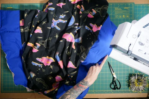 A printed lining being sewn to a blue coat shell at a sewing machine.