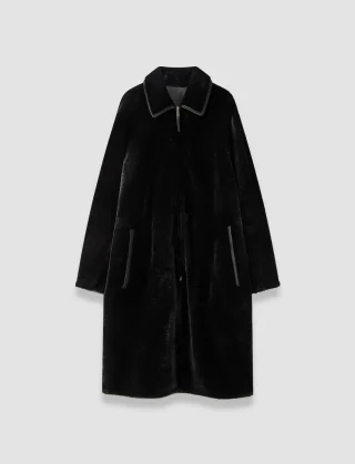 A long black shearling-look coat showing the fleece side, with a collar and front zip.
