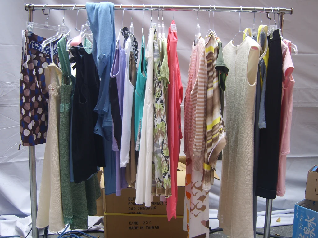 A rolling rack of women's dresses and tops in front of a white backdrop, cartons stacked beneath it.