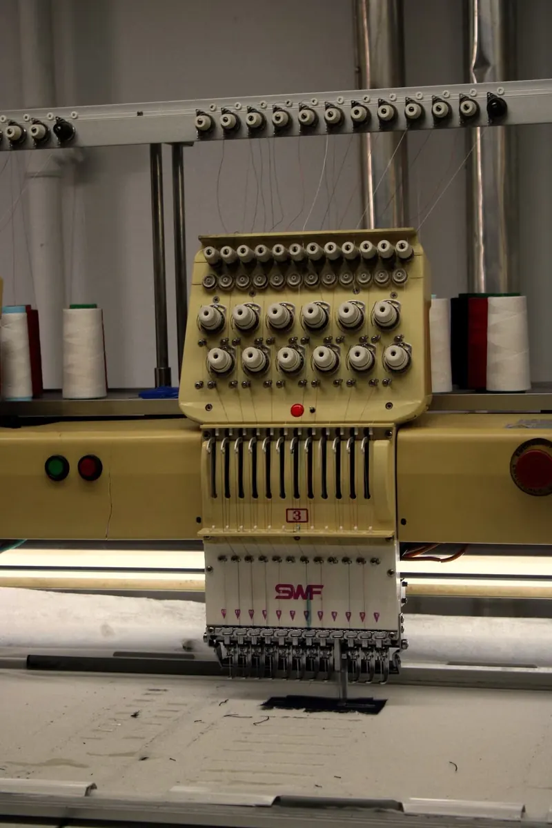Needles and thread on an industrial embroidery machine above a fabric panel.