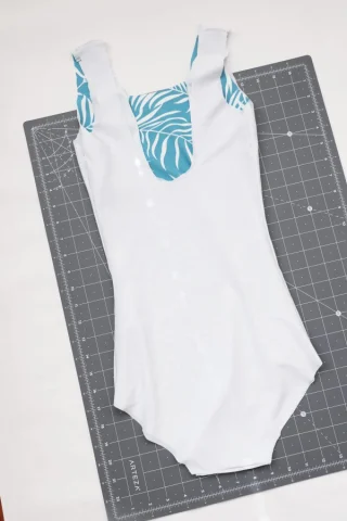 A one-piece swimsuit turned inside out on a cutting mat, its white lining facing up and the printed outer fabric showing at the neckline.