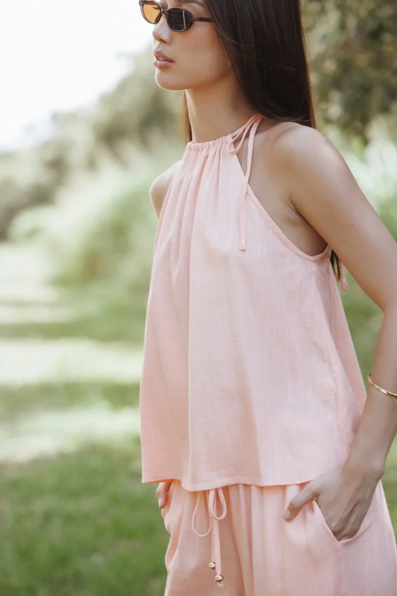A woman outdoors in a pale pink halter top with a gathered neckline and matching trousers.