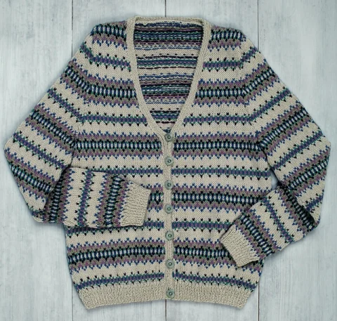 A V-neck cardigan in a blue, grey and cream Fair Isle pattern laid flat on wooden boards.