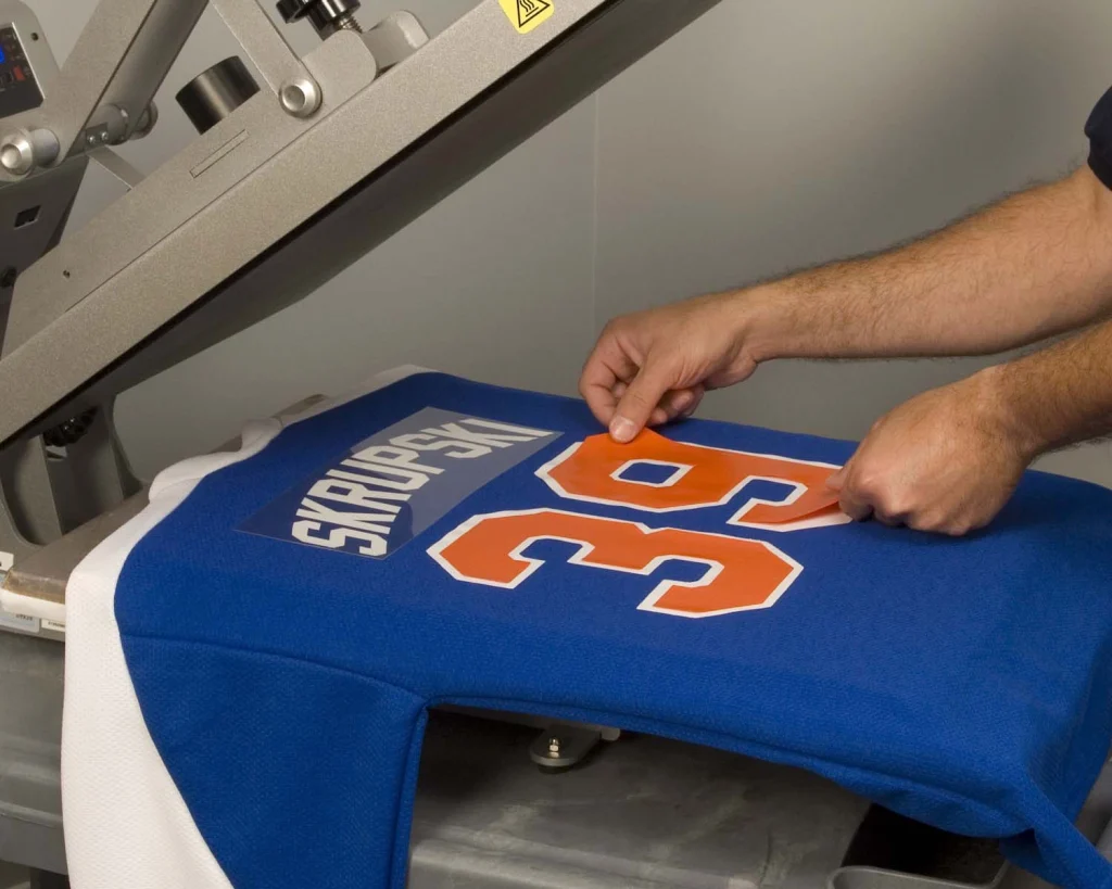 A worker lining up an orange number 39 on a blue jersey in a heat press.