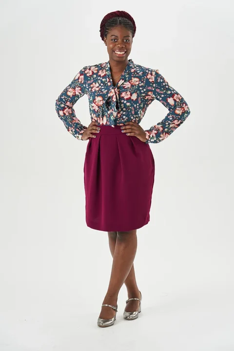A plum tulip skirt with slanted front pleats, worn with a floral blouse.