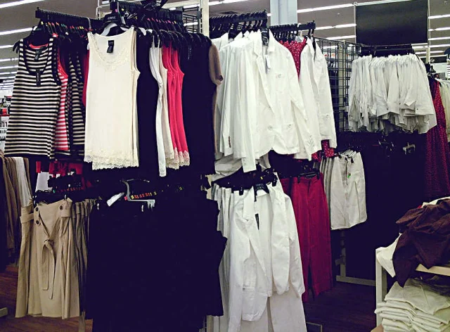 Racks of striped tank tops, white shirts and red trousers on a store sales floor.