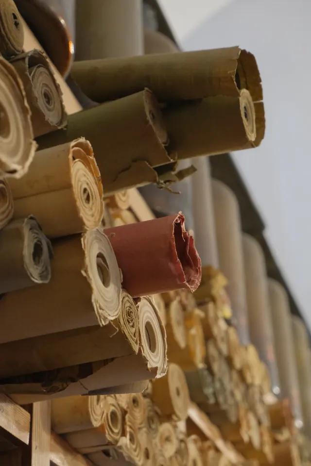 Rolls of fabric in beige, olive and brown paper wrapping stacked on wooden shelves.