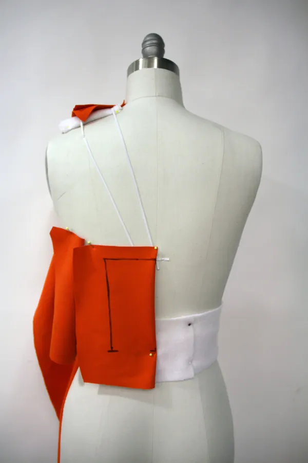 Trial bodice fabric pinned to a dress form, with construction lines marked on it.